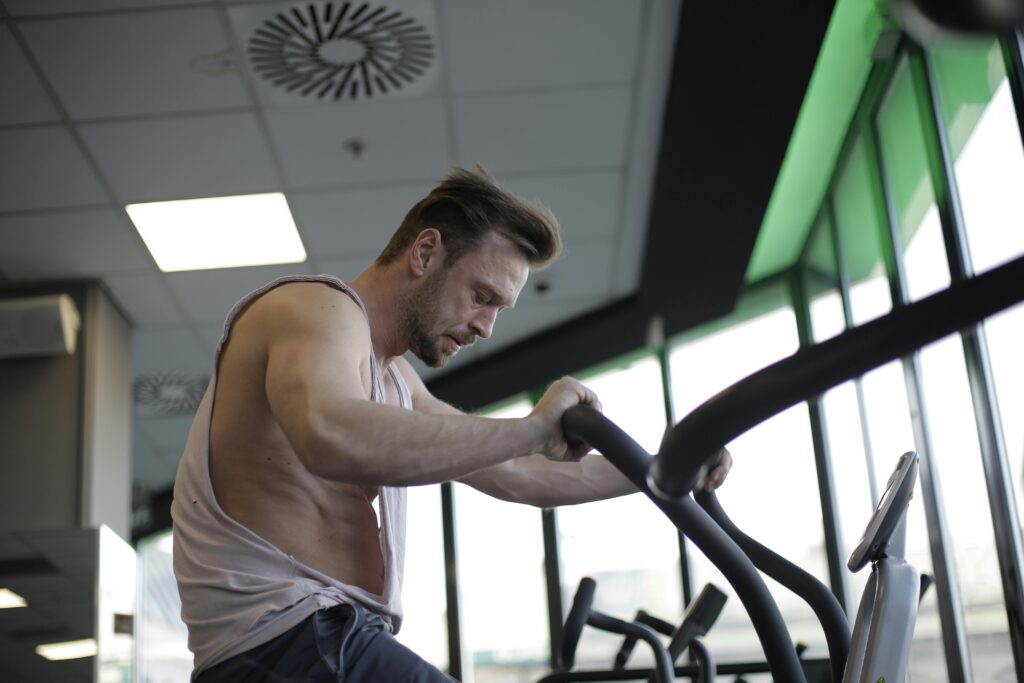 A muscular man working out vigorously on an elliptical in a modern gym setting.